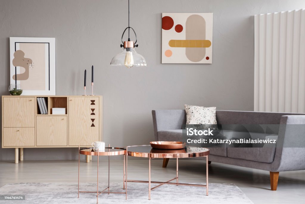 Abstract paintings on a gray wall of a classy living room interior with a wooden sideboard and shiny golden coffee tables Living Room Stock Photo