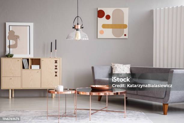 Abstract Paintings On A Gray Wall Of A Classy Living Room Interior With A Wooden Sideboard And Shiny Golden Coffee Tables Stock Photo - Download Image Now