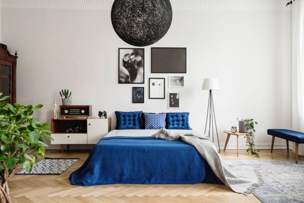black chandelier in navy blue bedroom in tenement house. floor lamp between king size bed and small table with pot and clock on it. real photo concept - bedding bedroom duvet pillow imagens e fotografias de stock