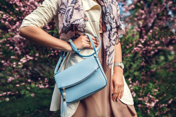 Young woman holding stylish handbag and wearing trendy outfit. Spring female clothes and accessories. Fashion Young woman holding stylish blue handbag and wearing trendy outfit in garden. Spring female clothes and accessories. Fashion handbag stock pictures, royalty-free photos & images