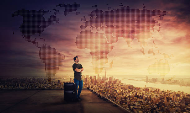 Man dreamer standing with suitcase on the rooftop of a skyscraper, smiling looking over city horizon. Thoughtful businessman planning his next holiday destination. World map hologram projection.