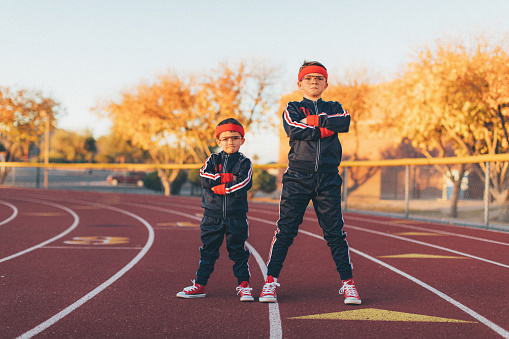 A young team of nerd boys are dressed in retro track suits and headbands stand on the running track ready to out exercise the competition. They are eager to stretch and exercise while finding their inner mojo. Image taken in Tempe, Arizona.