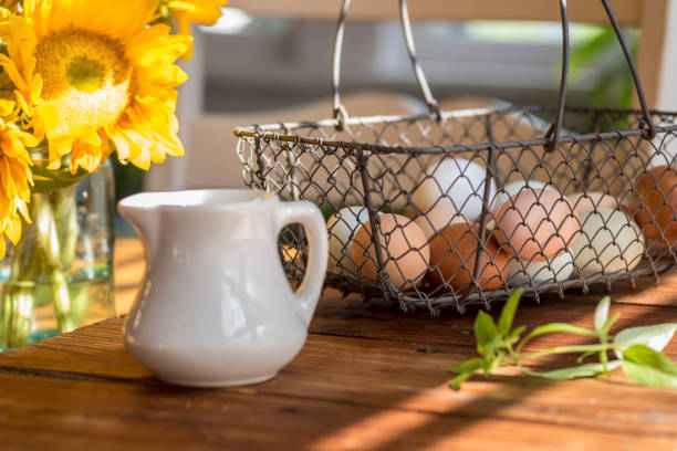 Multi colored fresh eggs in wire basket on rustic wood table in natural sunlight