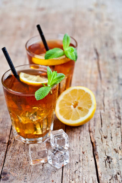 istock Cold iced tea with lemon, mint leaves and ice cubes in two glasses on rustic wooden table background. 1146777607