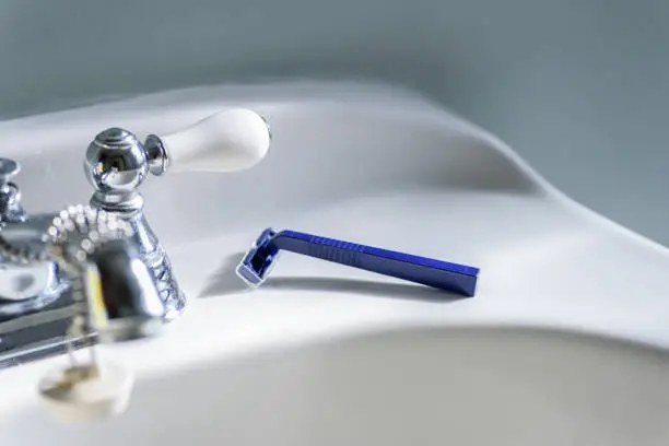 Blue disposable razor on white sink in bathroom