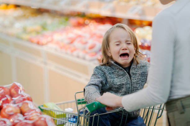 Child crying in shopping cart in supermarket Young boy child crying temper tantrum in shopping cart with mother parent in produce section aisle of supermarket growing pains children misbehaving stock pictures, royalty-free photos & images