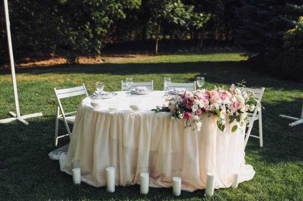 istock Table setting. A large white long table, decorated with flowers, with plates, glasses and forks, stands in a park with green grass. Wedding decorations and details. Wedding party outdoors. 1146782902