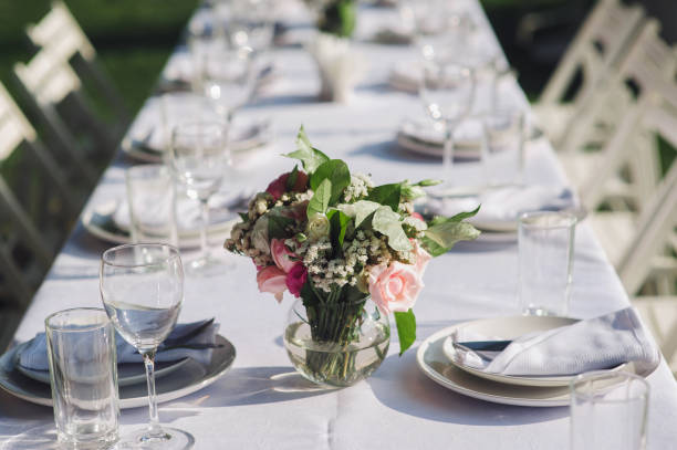 istock A large white long table with chairs, decorated with fresh flowers, with plates, glasses and forks, stands in a park with green grass. Wedding decorations and details. Preparing for a wedding party. 1146782907