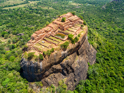 Aerial view from above of Sigiriya or the Lion Rock, an ancient fortress and a palace with gardens, pools, and terraces atop of granite rock in Dambulla, Sri Lanka. Surrounding jungles and landscape.