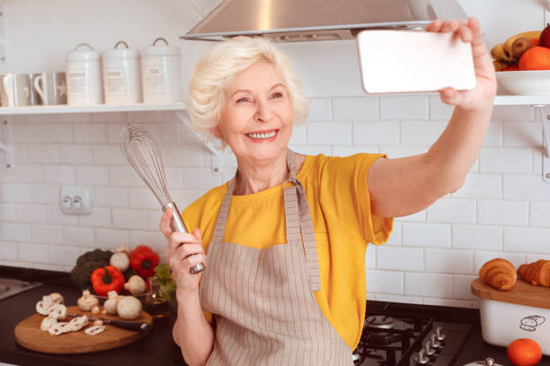 Grandmother makes selfie with a whisk in the kitchen.