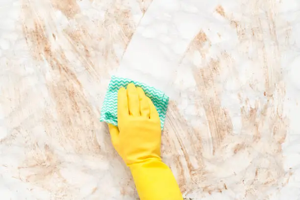 Hand wearing a glove, wiping clean a dirty marble counter or floor with a paper towel
