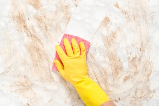 Hand wearing a glove wiping clean a dirty marble counter or floor with a sponge