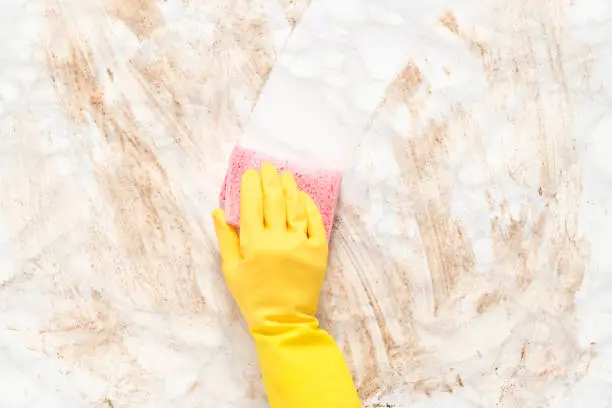Gloved hand wiping clean a dirty marble floor or counter with a sponge