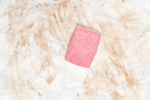 Overhead view of a pink sponge wiping clean a dirty marble floor or counter