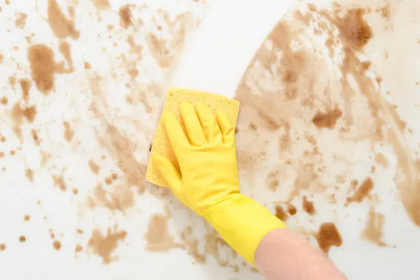 Gloved hand wiping a dirty counter top or floor with a yellow sponge