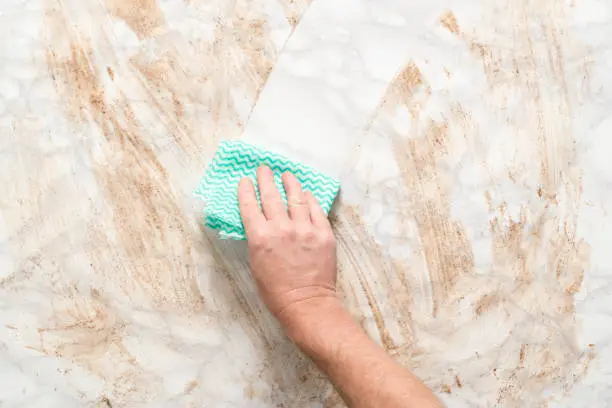 Hand wiping clean a dirty marble surface with a paper towel
