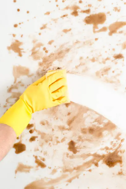 Hand wearing a glove wiping a dirty counter or floor with a sponge