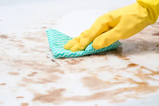 Hand wearing a glove wiping spills on a counter top or floor with a cloth or rag