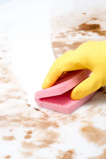Gloved hand wiping spills on a counter or floor with a pink sponge