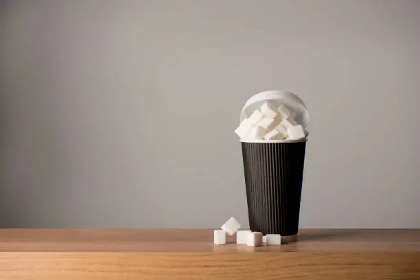 Tall paper coffee cup overflowing with sugar cubes on a wooden surface, copy space