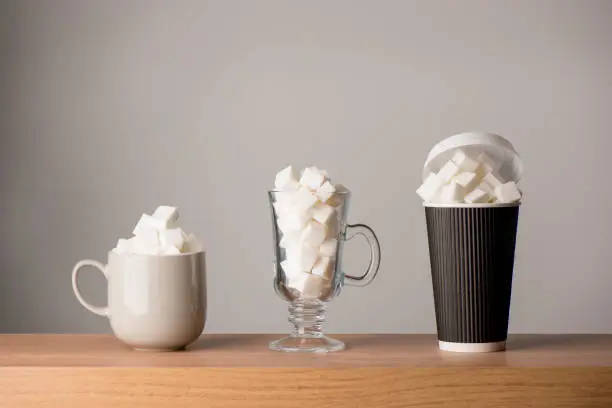 Coffee mug, latte glass, and tall paper cup all filled with sugar cubes