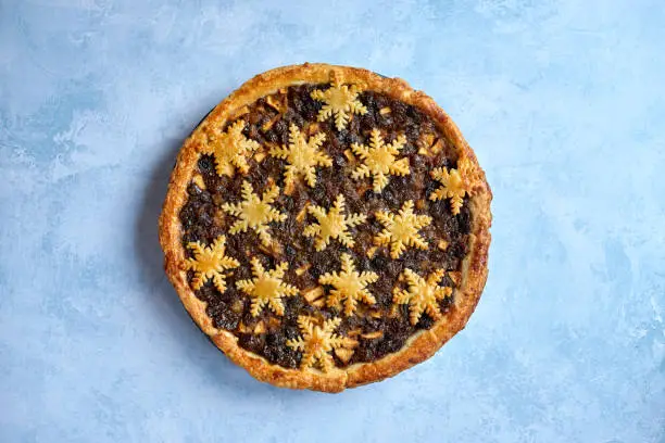 Large whole mince pie centered on blue stone background, traditional British Christmas food