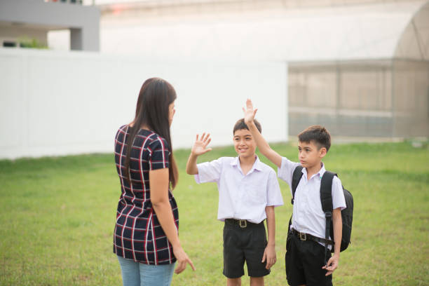 istock Mother taking sons to school together, hand wave say good bye 1146818084