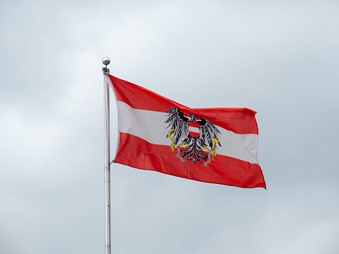 Austrian Flag with the Federal Eagle Coat of Arms and Red, White and Red Colors flying on a Grey Background