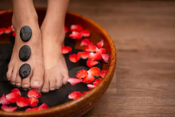 Closeup shot of a woman feet dipped in water with petals in a wooden bowl. Beautiful female feet at spa salon on pedicure procedure.