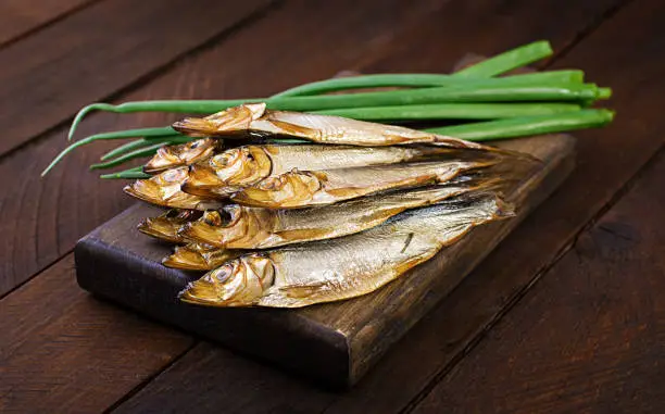 Photo of Smoked sprat and green onion  on a cutting board on a wooden background. Smoked fish.