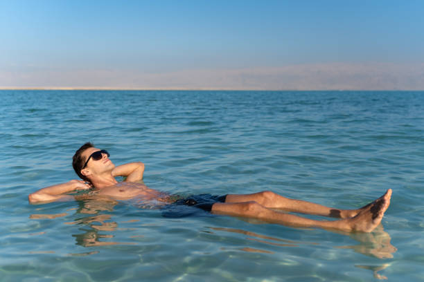 young man floating on the water surface of the dead sea man taking a tan and relaxing in the dead sea. holiday concept desert wash stock pictures, royalty-free photos & images
