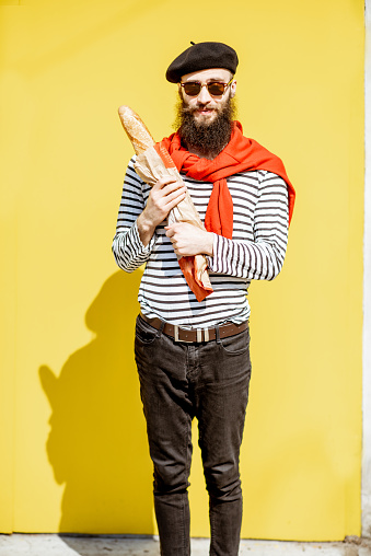 Portrait of a stylish man dressed in french style with striped shirt, hat and red scarf on the yellow background