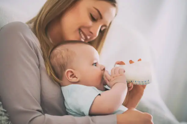 Happy mother is feeding her baby boy at home.