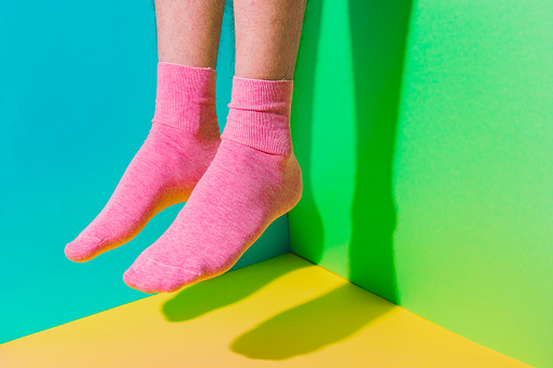 Male feet with hairy skin in socks flying  in the air above bold background in the corner with strong shadows. Minimal art concept. Body part