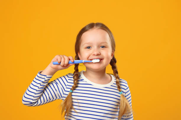 mała dziewczynka w pasiastej piżamie mycie zębów szczoteczką do zębów. koncepcja codziennej higieny. żółte tło. - pigtails zdjęcia i obrazy z banku zdjęć