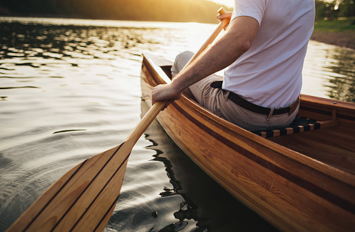 Close up of man holding canoe paddle at sunset lake.