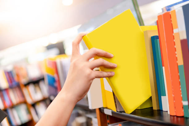 ベストセラー出版コンセプト。男性の手を選択し、書店で木製の本棚から黄色の本を選びます。大学公立図書館における教育研究 - bookshelf book reference book choosing ストックフォトと画像