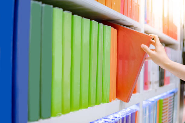 istock Male hand choosing new green ring binder file folder from colourful shelf display in stationery shop. Buying office supplies concept 1146867358