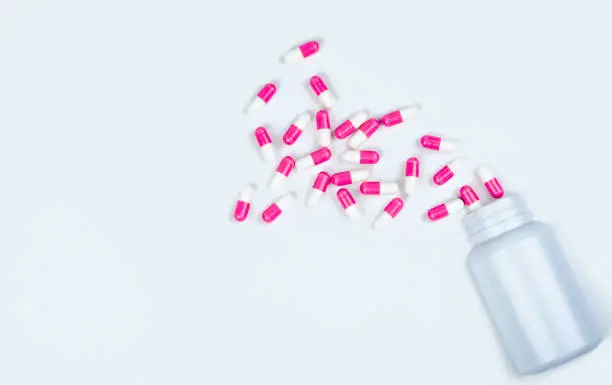 Pink-white capsule pills spread out of drug bottle. Antipsychotic drug. Capsule medicine for treatment depression. Anti-anxiety drug. Global healthcare. Pharmacy background. Pharmaceutical industry.