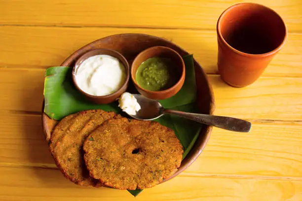 Top view of thalipith popular Maharashtrian savory pancakes with curd and pudina Chutney served in clay utensils