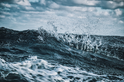 Wave rocks crashing exploding white ocean sea water spray power into blue sky along rocky coastline close-up Photograph.