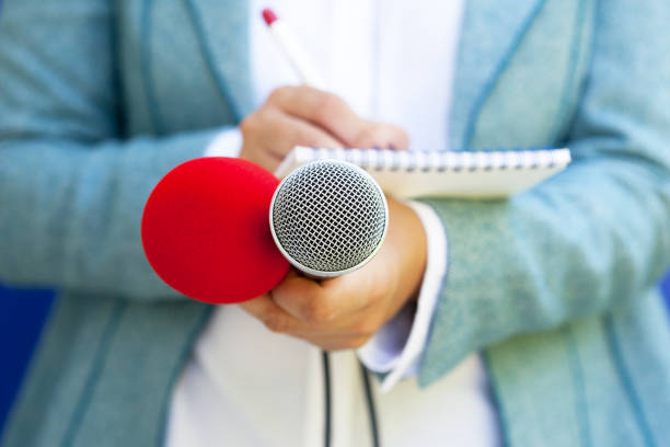 istock Female reporter at press conference, writing notes, holding microphone 1146884659