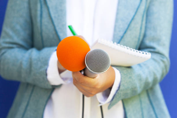 istock Journalist at news conference, taking notes, holding microphone 1146885043