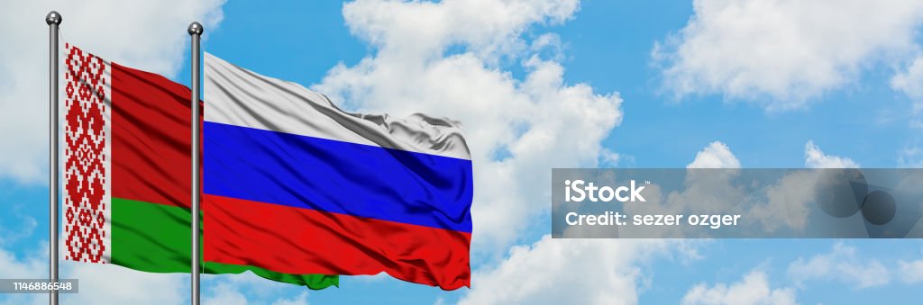 ベラルーシとロシアの旗は一緒に白い曇りの青空に対して風に手を振っています。外交概念、国際関係 - ベラルーシ共和国のロイヤリティフリーストックフォト