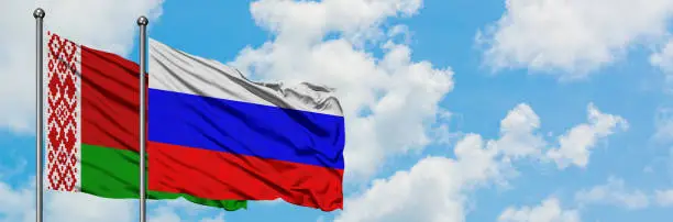 Photo of Belarus and Russia flag waving in the wind against white cloudy blue sky together. Diplomacy concept, international relations.