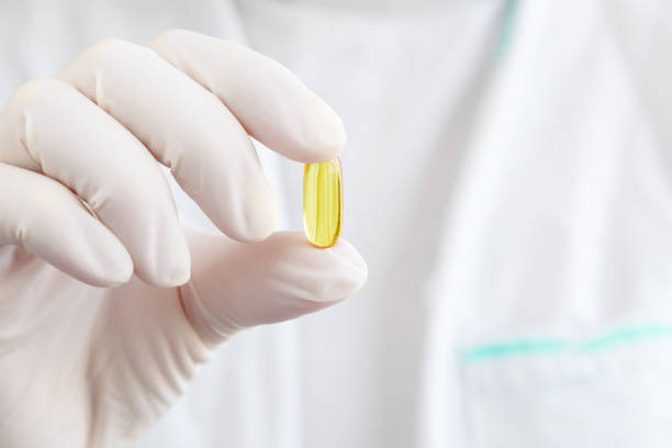 doctor hand in rubber protective glove holding yellow fish oil capsule. medical and pharmacy concept. front view. closeup. - fish oil cod liver oil doctor holding imagens e fotografias de stock