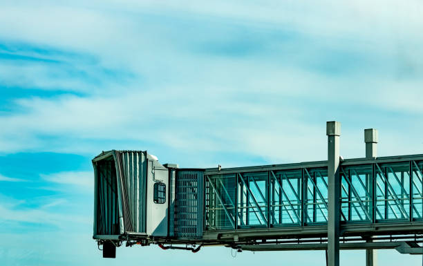 ponte jet dopo compagnia aerea commerciale decollare in aeroporto contro cielo blu e nuvole bianche. aereo passeggeri imbarco ponte ormeggiata. volo di partenza della compagnia aerea internazionale. ponte a getto vuoto. - passenger boarding bridge foto e immagini stock