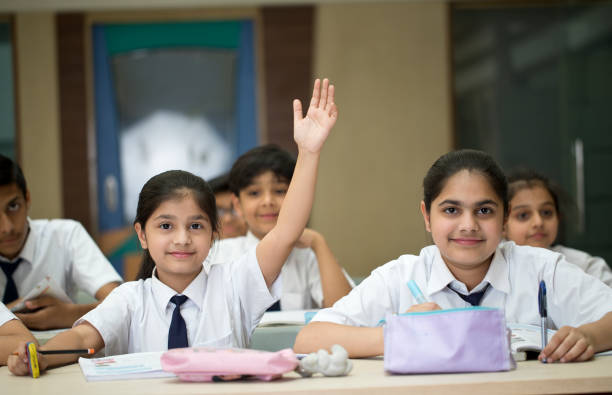 Girl raising hand in classroom Smiling girl raising her hand to answer a question in classroom boy and girl looking at camera stock pictures, royalty-free photos & images