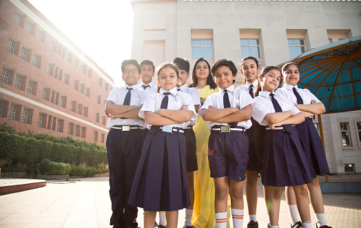 Group of schoolgirls and schoolboys posing with teacher in school courtyard