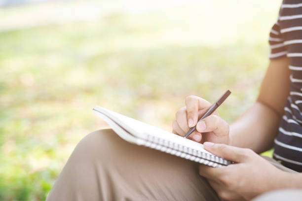istock close up hand young man are sitting on a marble chair. using pen writing Record Lecture note pad into the book in park public. 1146901824
